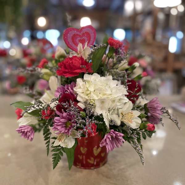 Mixed pink, white, and purple flowers in a red heart-patterned container