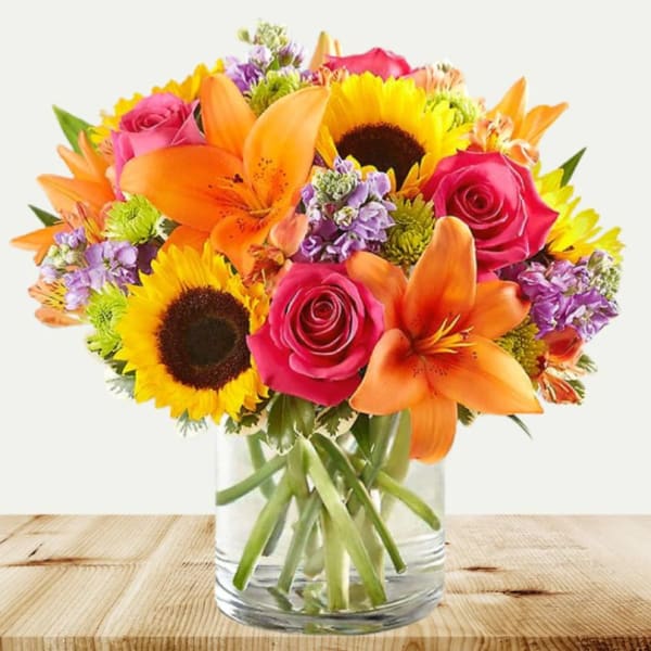 Bouquet of orange lilies, pink roses, and sunflowers in a glass vase