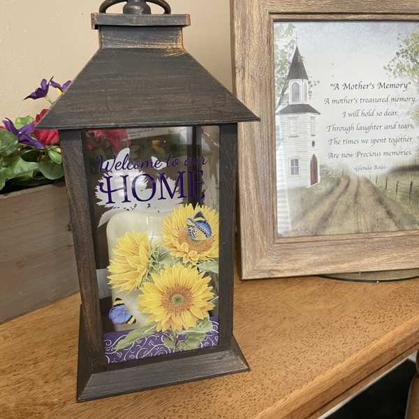 Decorative lantern with sunflower artwork and a memorial frame beside it