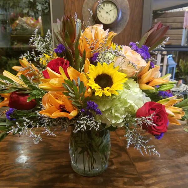 Mixed bouquet with sunflower, orange lilies, red roses, and hydrangea in a clear glass vase