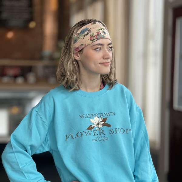 Woman wearing a turquoise flower shop sweatshirt and floral headband