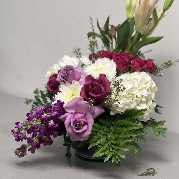 Mixed bouquet of roses, lilies, hydrangea, and purple flowers in a low vase