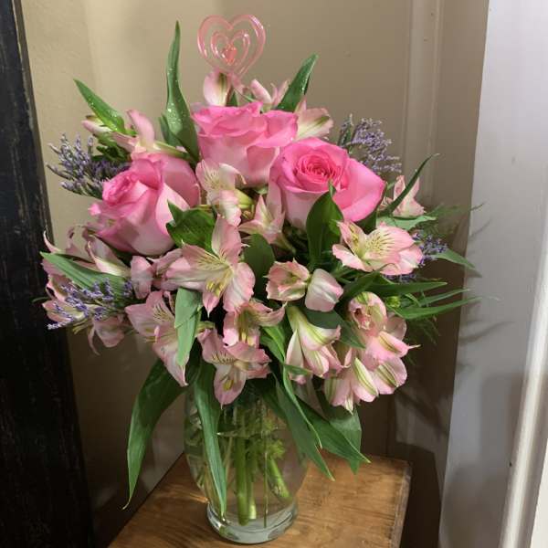 Pink roses and alstroemeria in a glass vase with a heart pick