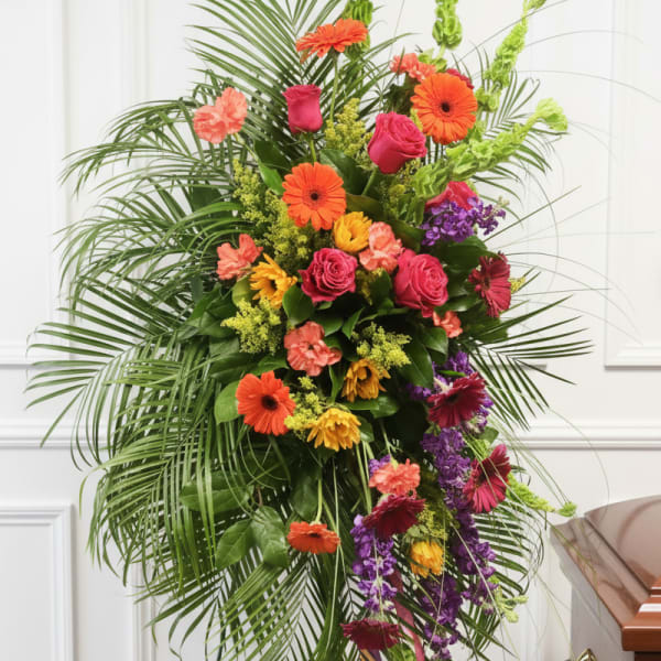 Tall standing spray with bright orange gerberas, pink roses, and purple flowers on an easel