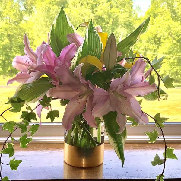 Pink lilies arranged in a gold vase with trailing ivy