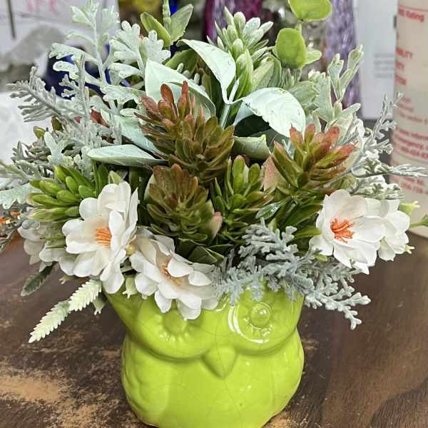 Artificial flowers arranged in a bright green owl-shaped planter