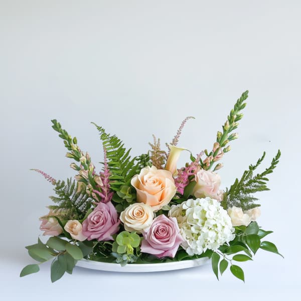 Pastel roses and white hydrangea arranged in a low white tray