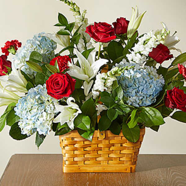Basket arrangement of red roses, blue hydrangeas, and white lilies