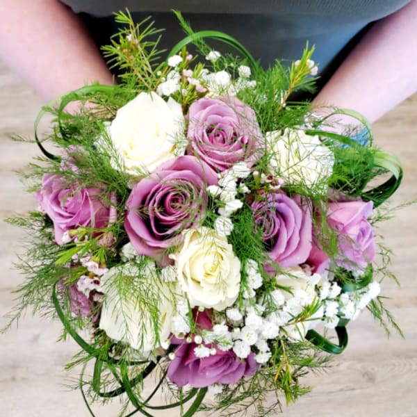Handheld bouquet of purple and white roses with airy greenery