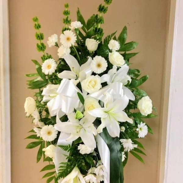 White floral standing spray with lilies, daisies, and ribbon on an easel