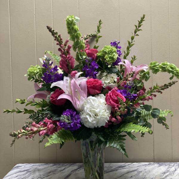 Tall mixed bouquet in a clear glass vase with pink, purple, white, and green blooms