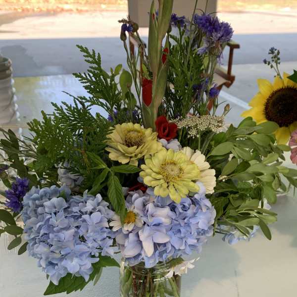 Mixed bouquet in a clear glass vase with blue hydrangeas and yellow daisies