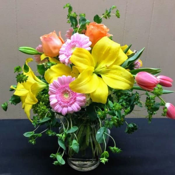Bouquet of yellow lilies, pink gerbera daisies, and roses in a glass vase