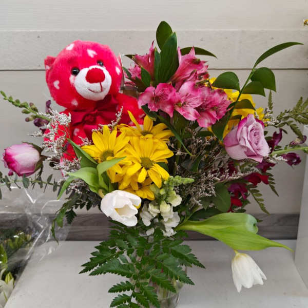 Bouquet of mixed flowers with a pink teddy bear in a glass vase