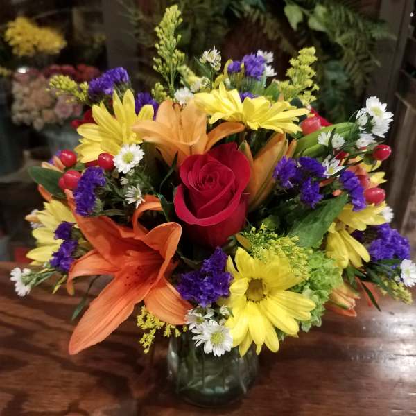 Mixed bouquet with a red rose, lilies, and yellow daisies in a glass vase