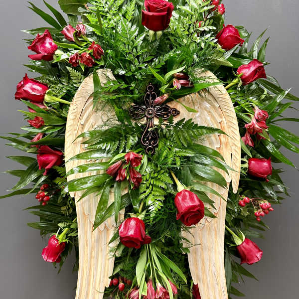 Standing floral spray with red roses and a wooden angel-wing cross