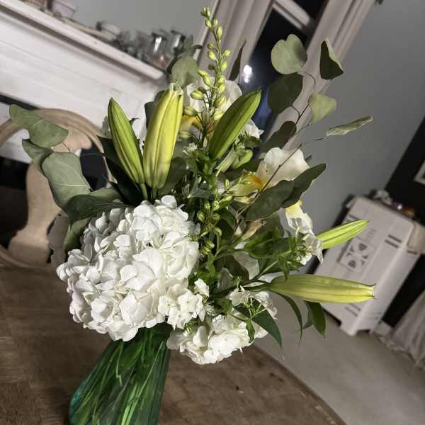 White hydrangeas and green lilies in a teal glass vase