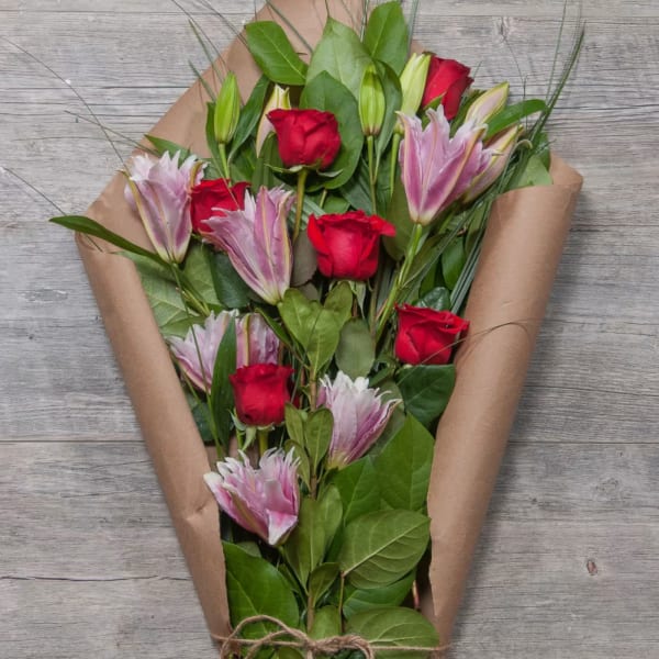 Bouquet of red roses and pink lilies wrapped in brown paper