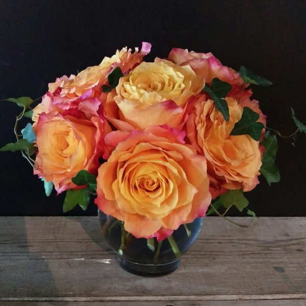 Orange and pink roses arranged in a clear glass vase