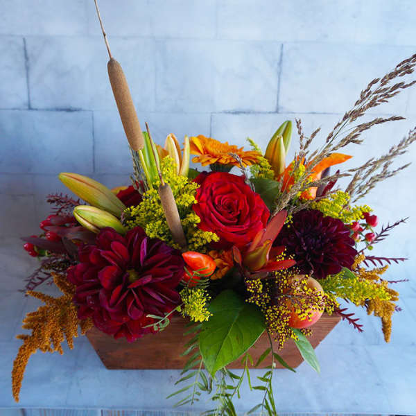 Autumn floral arrangement in a wooden box with red and orange blooms