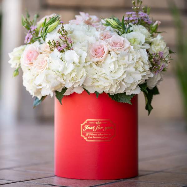 White and blush flowers arranged in a red hat box