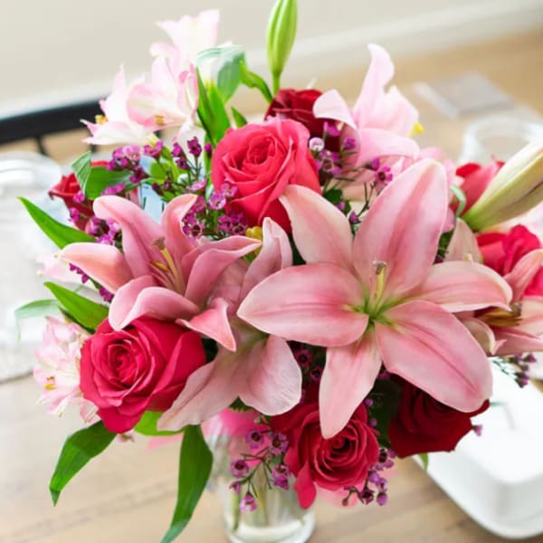 Pink lilies and red roses arranged in a clear glass vase
