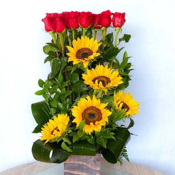 Tall arrangement of red roses and yellow sunflowers in a square vase