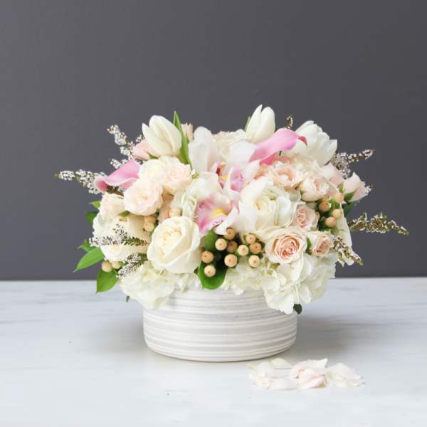 Pastel bouquet of roses, tulips, and calla lilies in a white striped vase