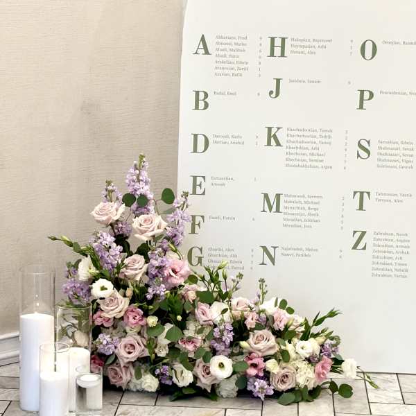 Pastel floral arrangement with roses and lavender blooms beside white candles