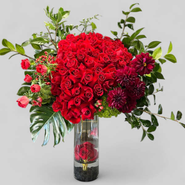 Red roses and burgundy flowers in a tall glass vase