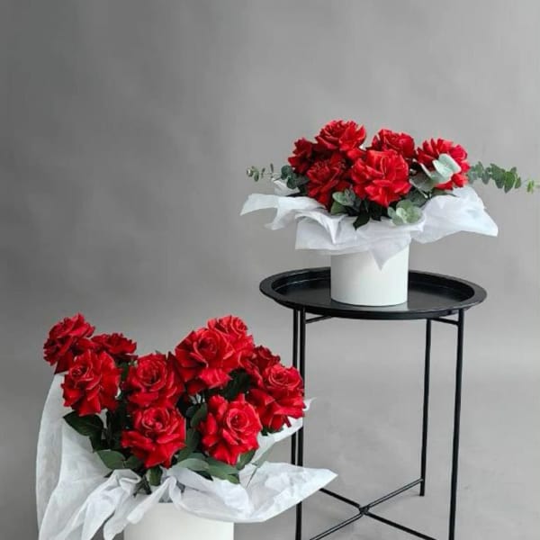 Two red rose bouquets in white wrapping, one in a white box and one on a stand