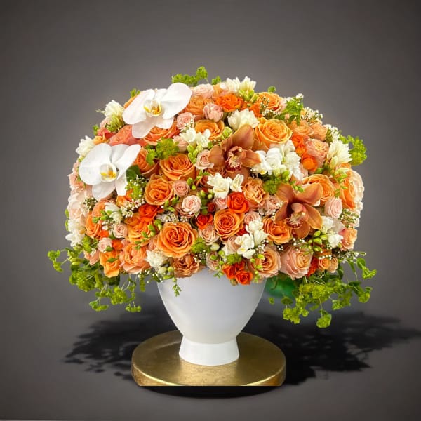 Large orange and peach floral arrangement in a white vase