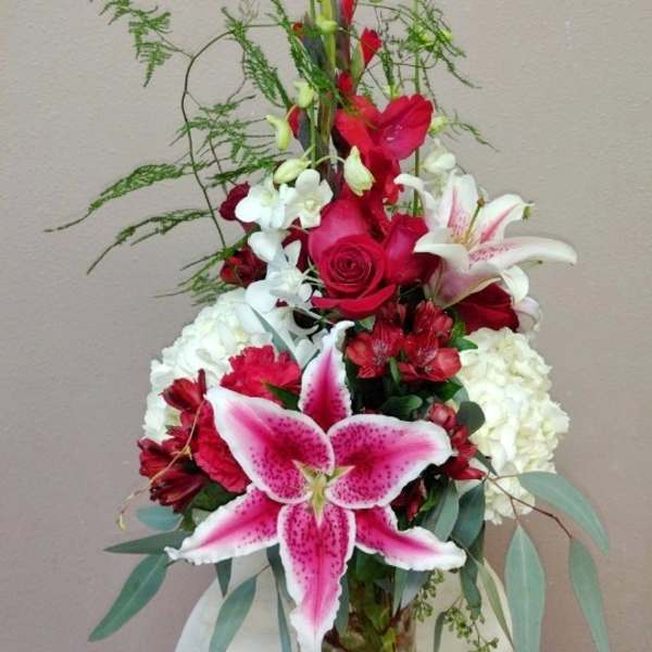 Tall red, white, and pink flower arrangement with lilies, roses, orchids, and hydrangeas in a clear glass vase.