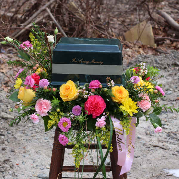 Colorful funeral spray around a dark urn with "In Loving Memory" text