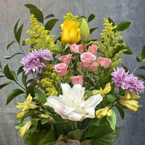 Mixed bouquet in a pink vase with roses, lilies, and purple blooms