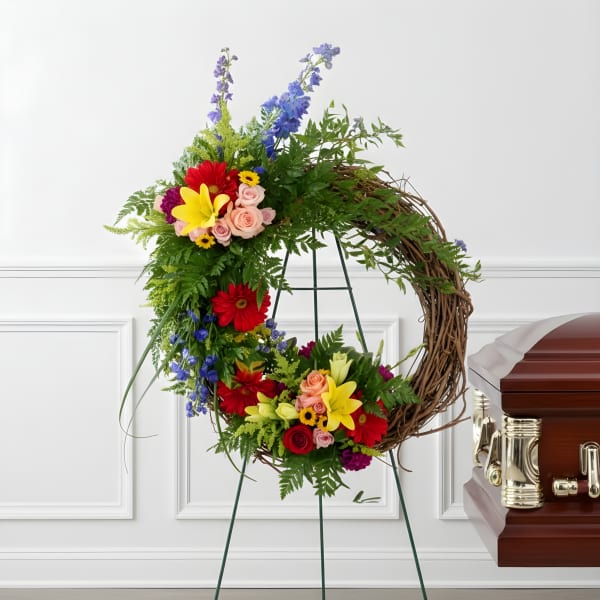 Colorful floral wreath on a stand beside a casket