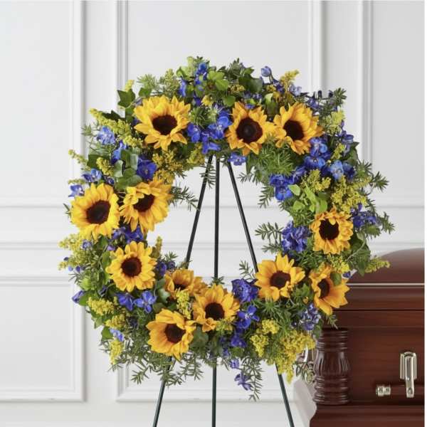 Sunflower and blue flower wreath on a standing easel beside a casket