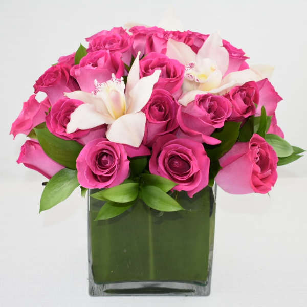 Pink roses and white orchids arranged in a square glass vase.