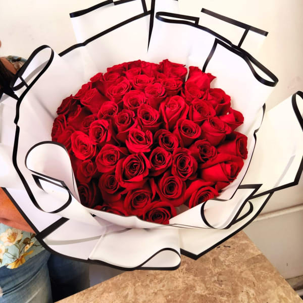 Large bouquet of red roses wrapped in white paper with black trim