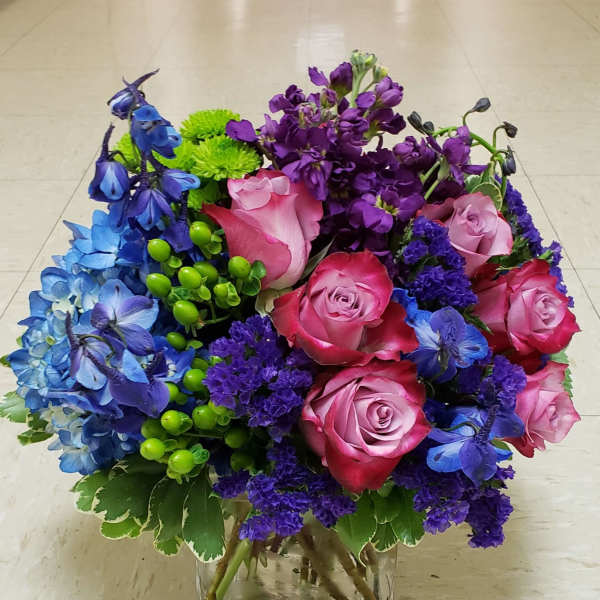 Bouquet of pink roses, blue and purple flowers in a clear glass vase