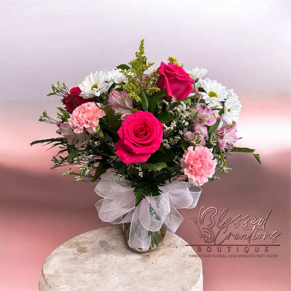 Vase arrangement of hot pink roses, pink carnations, and white daisies with a white bow.