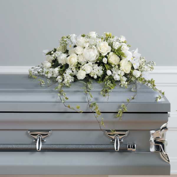 White floral casket spray with trailing greenery on a gray casket