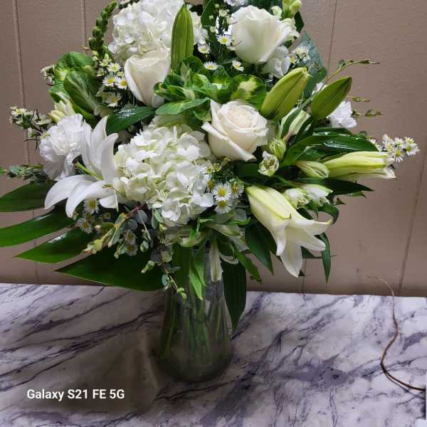 White roses, lilies, and hydrangeas arranged in a glass vase