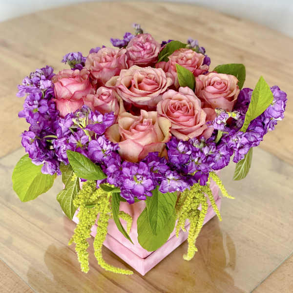 Pink roses and purple flowers arranged in a pink box