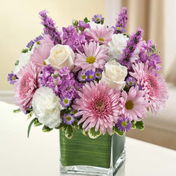 Pastel pink and lavender mixed flower arrangement in a square glass vase lined with green leaves
