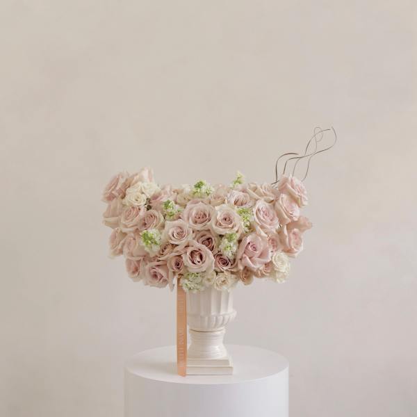 Blush roses and white flowers arranged in a white pedestal vase