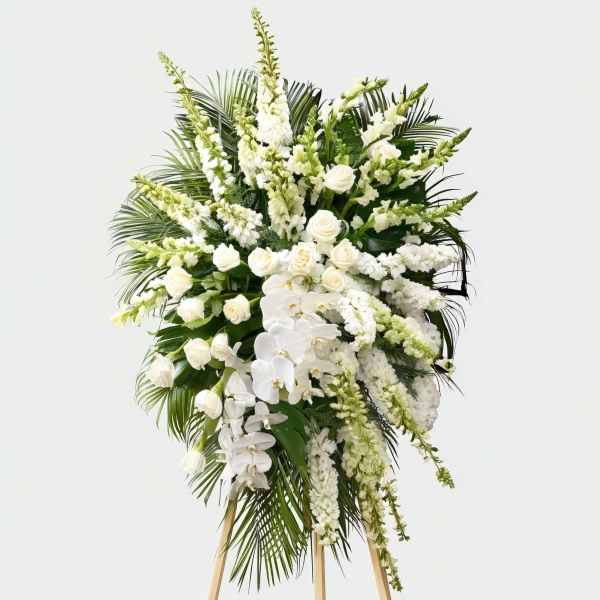 White floral standing spray with orchids and roses on a wooden easel