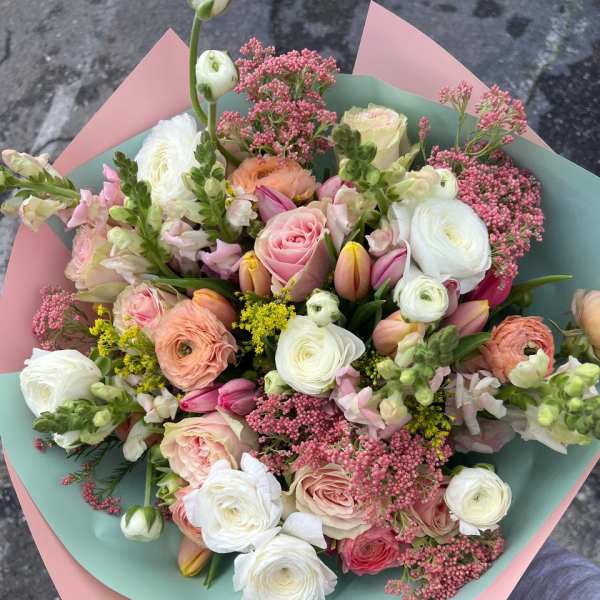Hand-tied bouquet of pink, white, and peach flowers wrapped in pastel paper