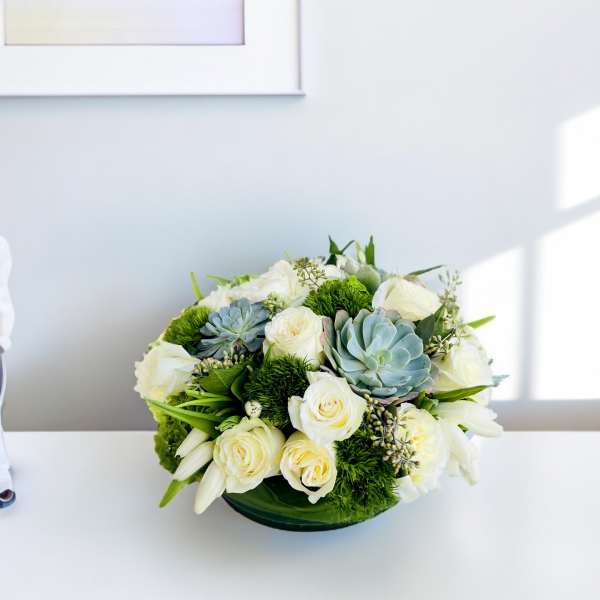 Round bouquet of white roses and blue succulents in a low container