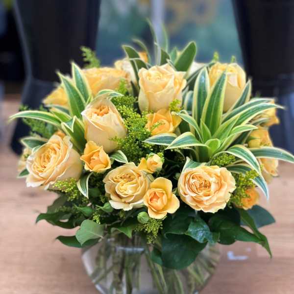 Peach roses in a clear glass vase with variegated foliage